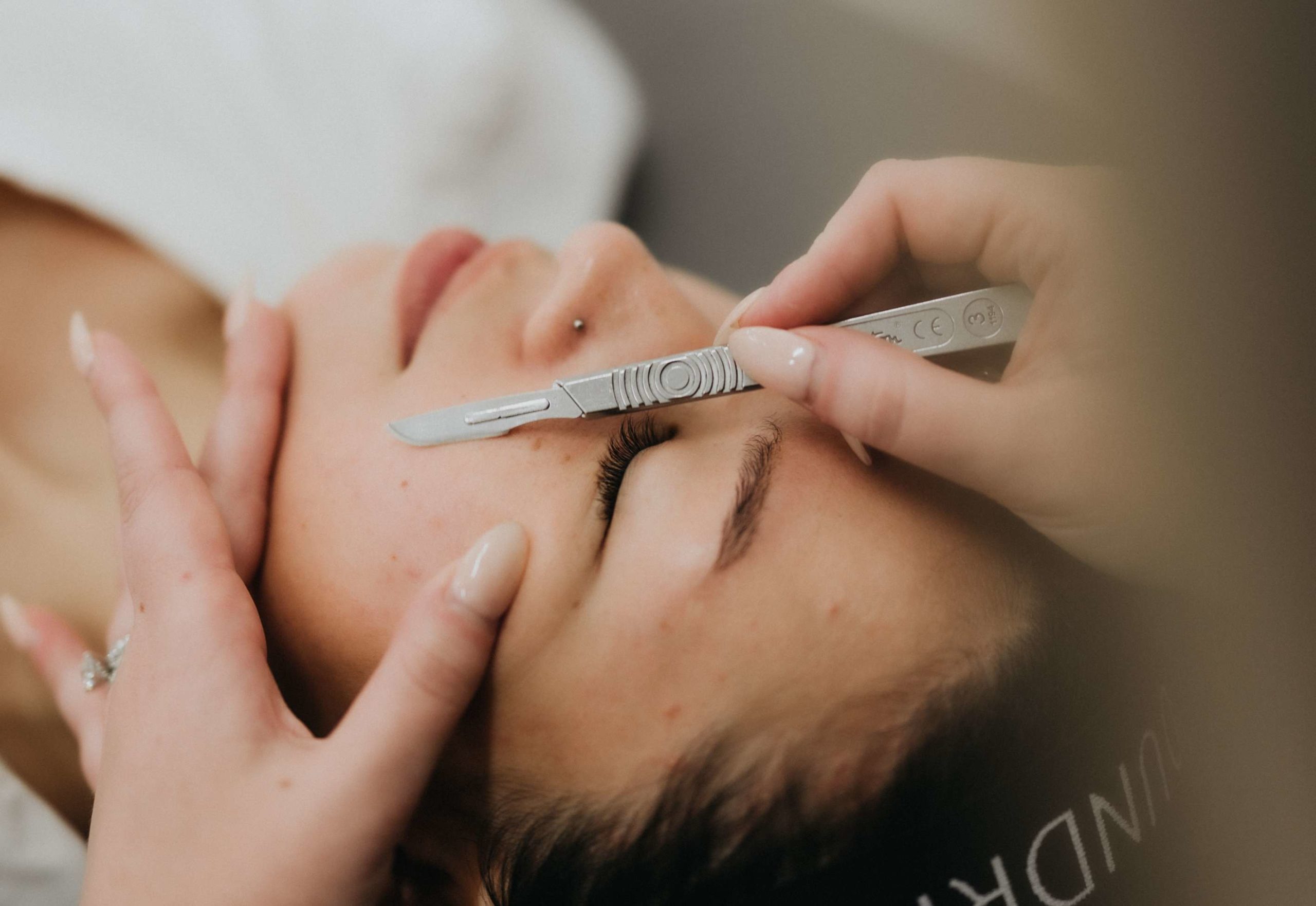 A woman in a facial salon having dermaplaning done to her face to remove hair and improve skin texture.